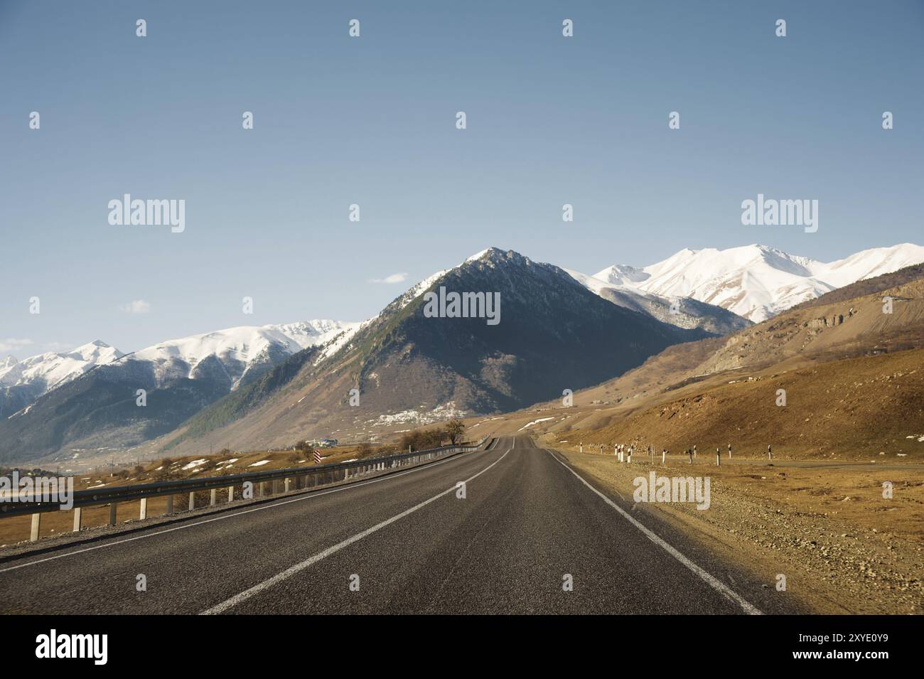 Blick auf die Herbststraße, die zu den Bergen führt, zu den schneebedeckten Gipfeln des Kaukasus. Das Konzept, mit dem Auto in die Berge zu fahren Stockfoto