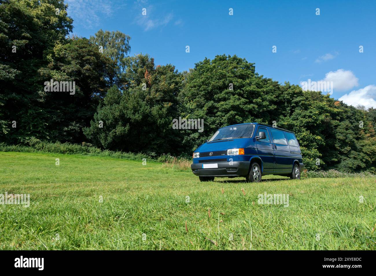 Ein entspannter Nachmittag mit dem Wohnmobil in einem üppigen grünen Feld, umgeben von lebendigen Bäumen unter einem breiten blauen Himmel Stockfoto