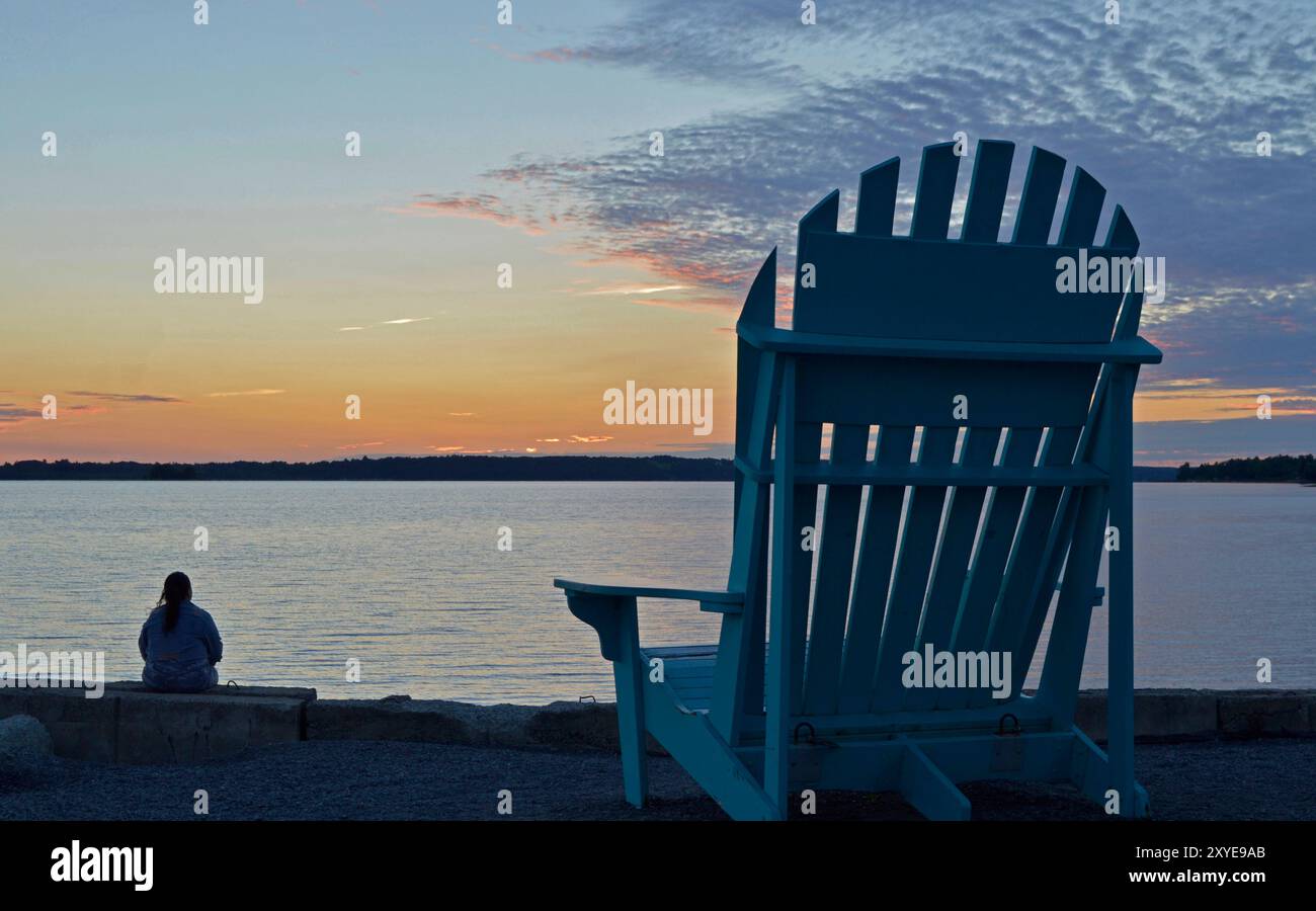 Eine Frau sitzt am Rande des Strandes und beobachtet den Sonnenuntergang im Spätsommer, eine sehr entspannende Umgebung Stockfoto