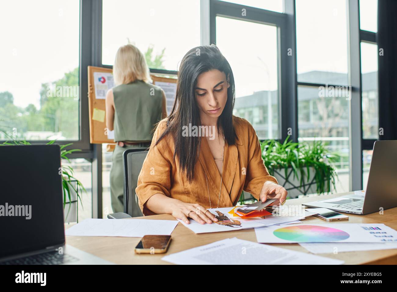 Eine Frau in einer leuchtend gelben Bluse untersucht eine Farbpalette, die bei der Arbeit in einem modernen Büro in Gedanken verloren geht. Stockfoto