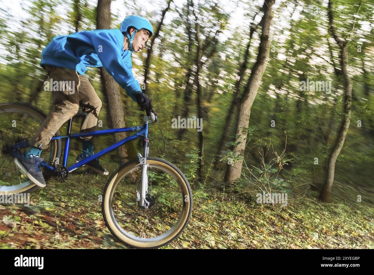 Ein junger Fahrer mit Helm und blauem Sweatshirt fliegt auf einem Fahrrad, nachdem er von einem hohen Kicker auf einem Waldradweg gesprungen ist. Aufnahmen mit langer Belichtung Stockfoto