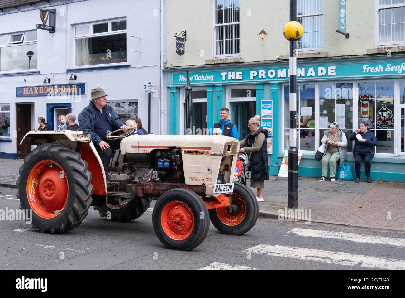 Mann mit Eimerhut, der einen roten David Brown 885 Traktor durch die Stadt fährt. Ballycastle, Großbritannien - 24. August 2024: Stockfoto