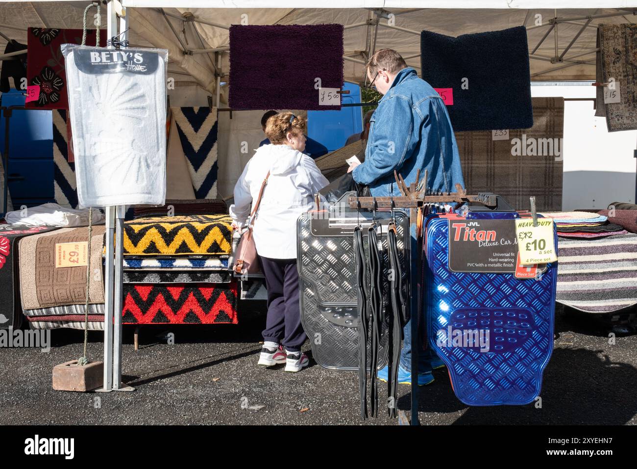 Verschiedene Teppiche und Matten zum Verkauf auf dem Freiluftmarkt, Männer und Frauen kaufen auf der jährlichen Messe Schnäppchen ein. Ballycastle, Großbritannien - 26. August 2024. Stockfoto