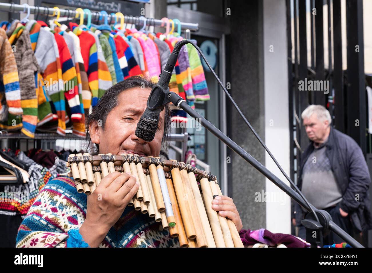 Mann in farbenfroher Spitze, der südamerikanische hölzerne Musikpfeifen auf der Straße spielt. Ballycastle, Großbritannien - 26. August 2024: Stockfoto