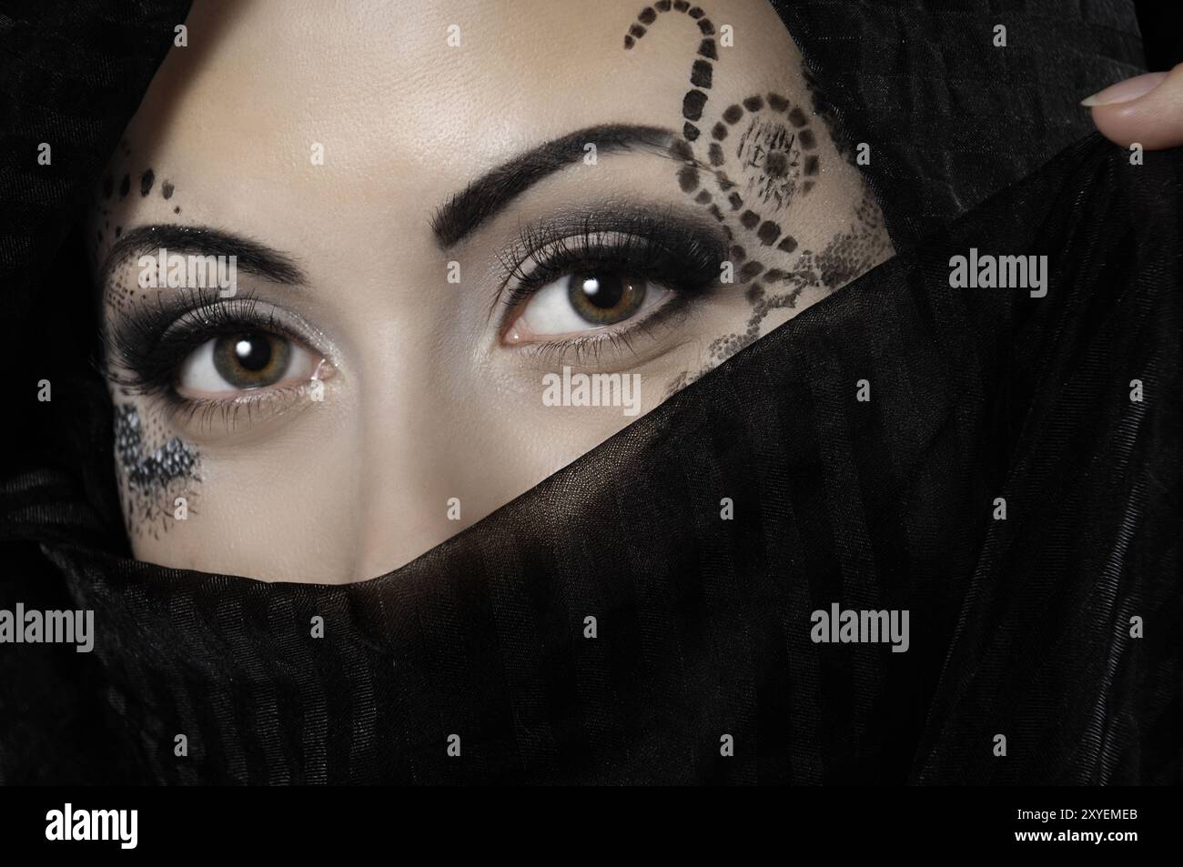 Exotisches Frauengesicht mit künstlerisch-temporärer Tätowierung, bedeckt mit schwarzem Kopftuch Stockfoto