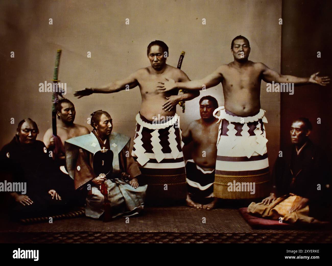 Japanische Sumo-Wrestler und Schiedsrichter, 1880 von Felice Beato Fotograf Japanisches handkoloriertes Schwarzweiß-Foto Japan Ende 19. – Anfang des 20. Jahrhunderts Vintage-Albumenfotografie ( Historic History ) digitale verbesserte Wiedergabe. (Zwei Wrestler tragen zeremonielle Schürzen, die mit Shimenawa verziert sind - Zickzack-Papierschlangen - Sumo-Ring tritt ein.) Stockfoto