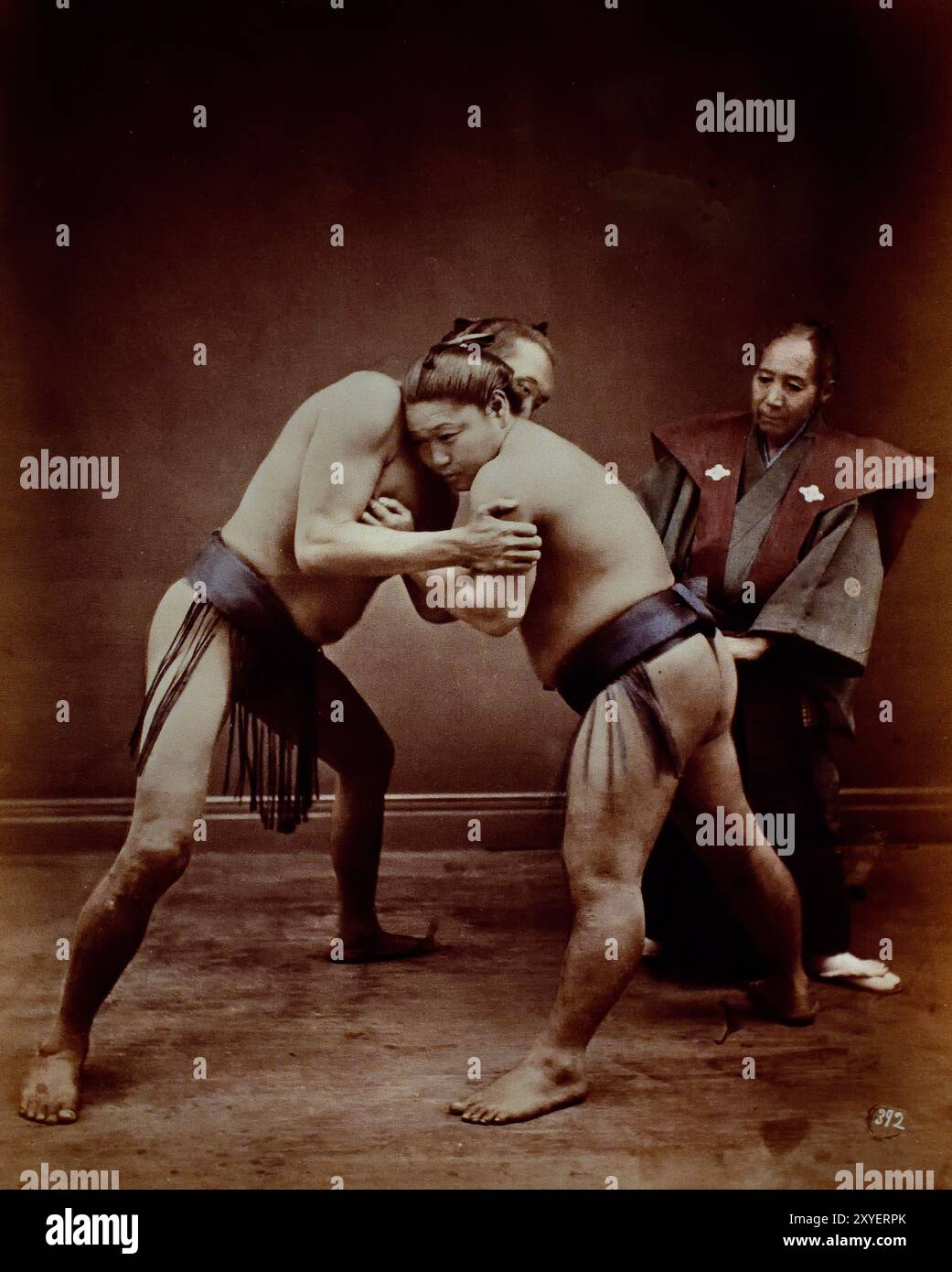 Zwei japanische Sumo Wrestler posierten mit Schiedsrichter, 1880 von Felice Beato Fotograf Japanisches handkoloriertes Schwarzweiß-Foto Japan Ende des 19. Jahrhunderts – Anfang des 20. Jahrhunderts Vintage Albumenfotografie ( Historic History ) digital verbesserte Reproduktion. Stockfoto