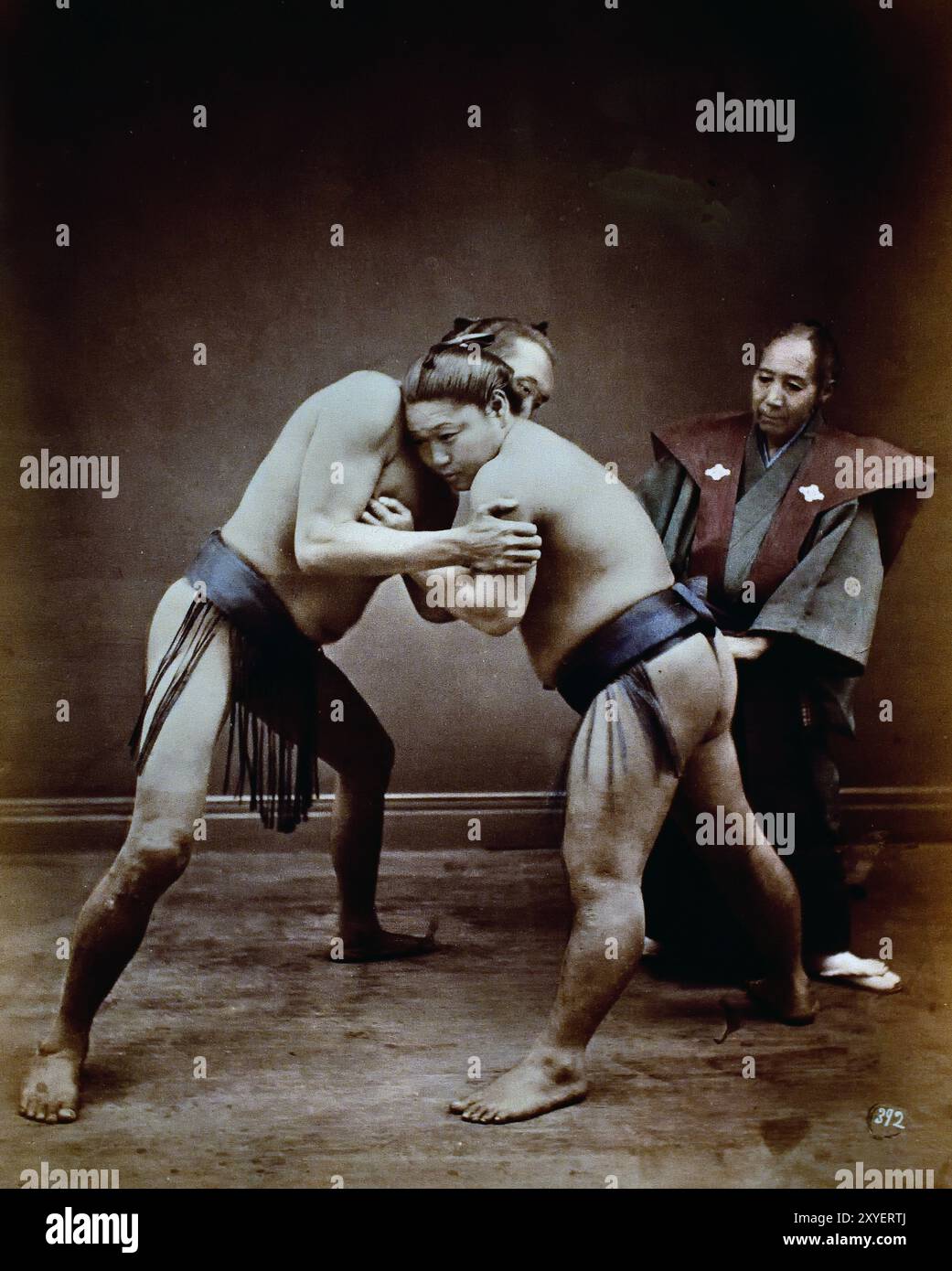 Zwei japanische Sumo Wrestler posierten mit Schiedsrichter, 1880 von Felice Beato Fotograf Japanisches handkoloriertes Schwarzweiß-Foto Japan Ende des 19. Jahrhunderts – Anfang des 20. Jahrhunderts Vintage Albumenfotografie ( Historic History ) digital verbesserte Reproduktion. Stockfoto