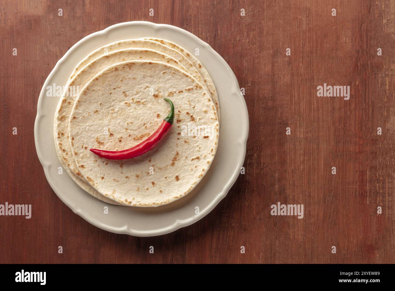 Eine Red Hot Chili Pepper, geschossen von oben auf einem Stapel Tortillas, mexikanische Fladen, auf einem dunklen Holzmöbeln im Landhausstil Hintergrund mit Kopie Raum Stockfoto