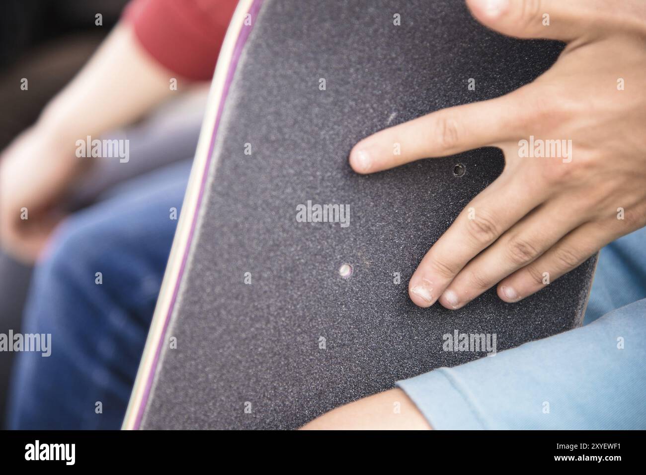 Ein kleiner Junge auf den Knien klebt das Griptape in Begleitung von Freunden bei sonnigem Wetter auf ein Skateboard. Vorbereitung eines Skateboards für einen Skatepark-Wettkampf Stockfoto