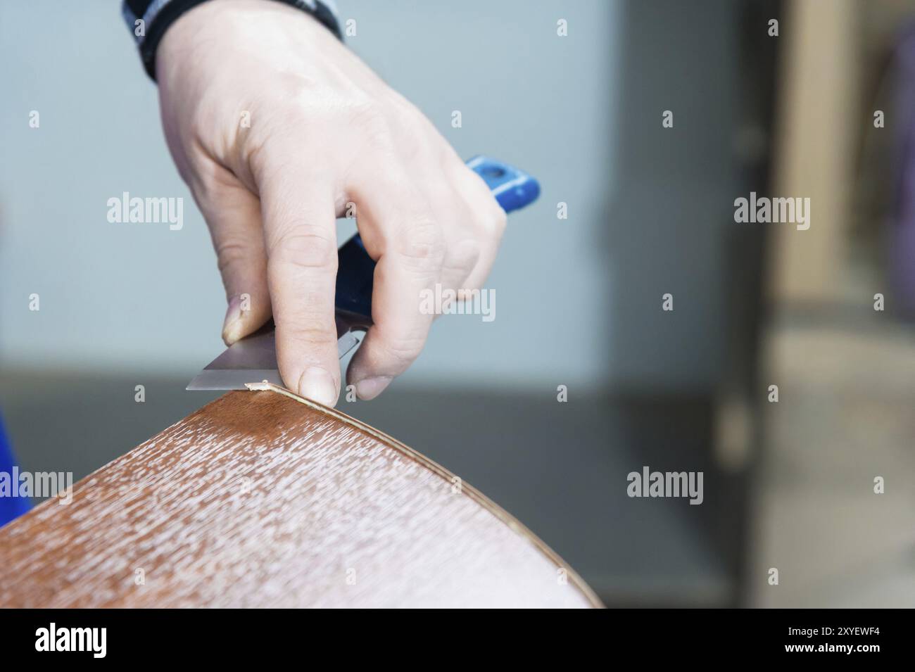 Eine Nahaufnahme der nicht gepflegten Hände des echten Zimmermanns rundet die Verarbeitung der Spanplattendetails der Möbel ab, indem sie die Kante abschneidet Stockfoto