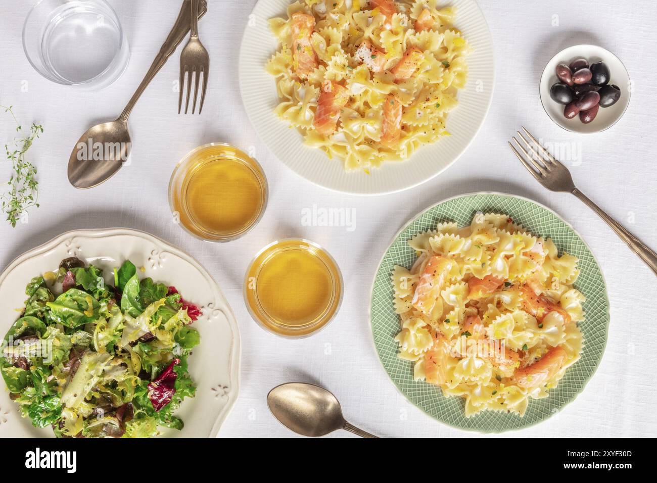 Zwei Platten von Lachs Nudeln. Farfalle mit geräuchertem Lachs und Sahnesoße, Schuß von der Oberseite mit Wein und Salat mesclun Blätter Stockfoto