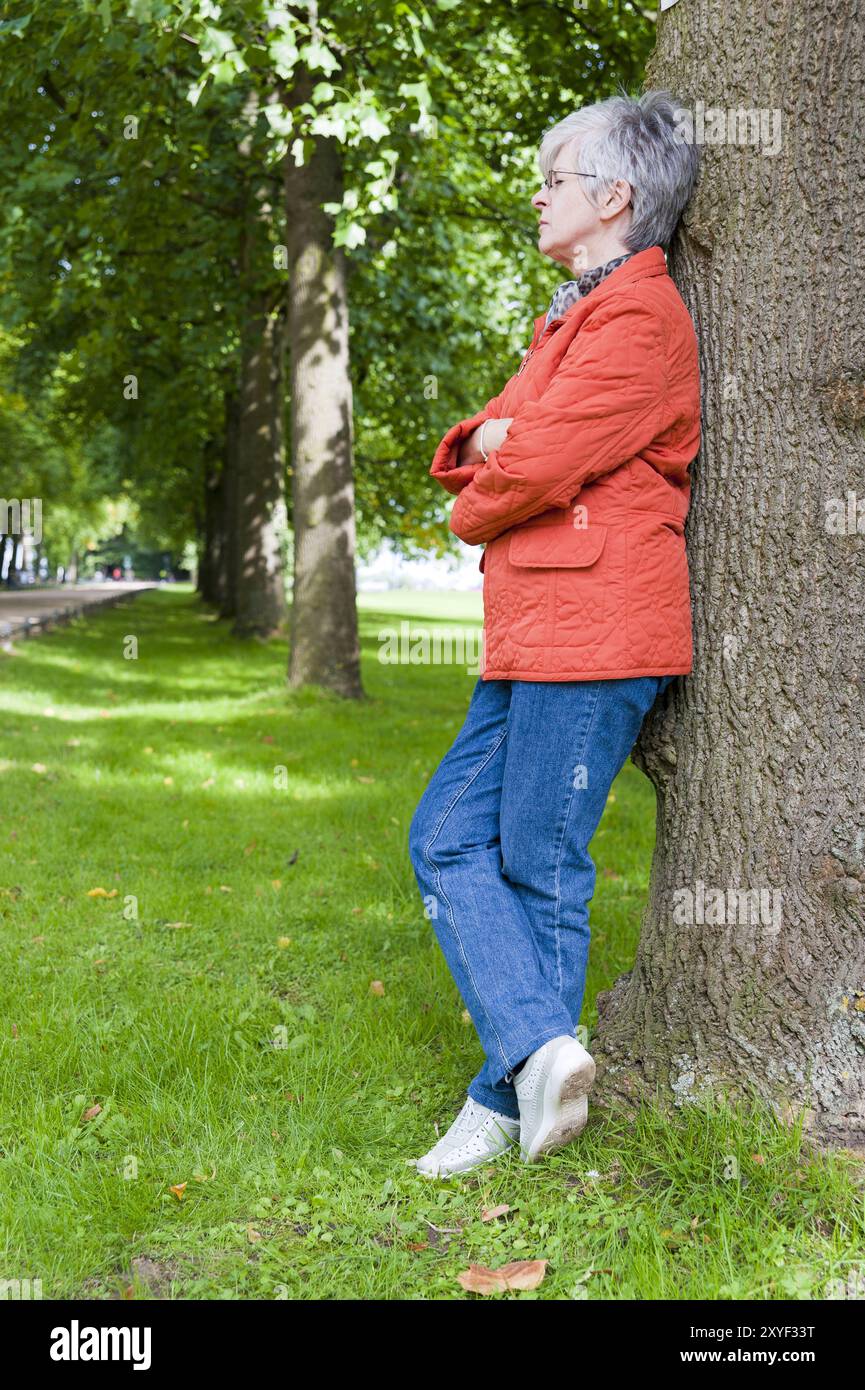 Frau, 50+, steht an einem Baum und ruht aus Stockfoto