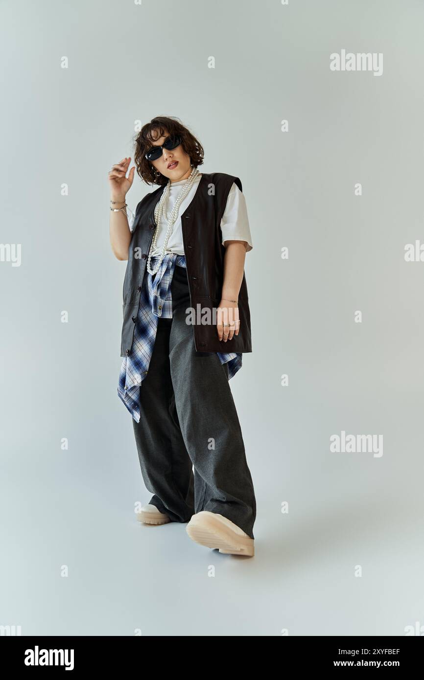 Eine Frau posiert selbstbewusst, trägt eine schwarze Weste über einem weißen T-Shirt und einer Hose mit weitem Bein. Stockfoto