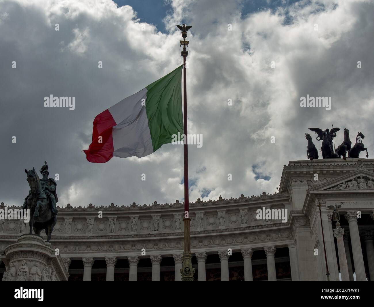 Italienische Flagge mit historischen Reiterstatuen auf einem großen Gebäude unter bewölktem Himmel, Rom, Italien, Europa Stockfoto