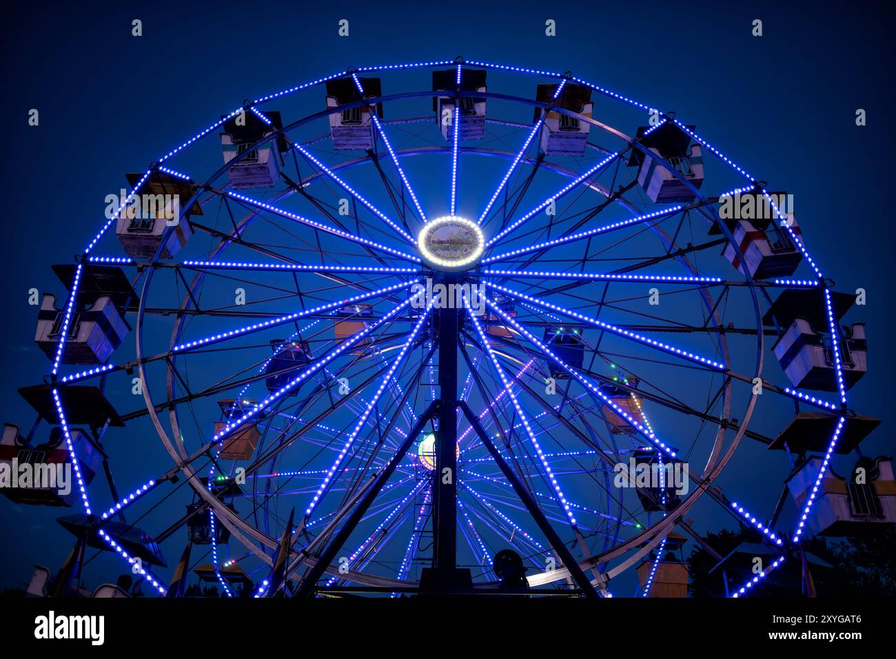 Riesenrad beleuchtet Arlington County Fair Arlington Virginia | ARLINGTON, Virginia — Ein lebhaft beleuchtetes Riesenrad leuchtet vor dem dunkler werdenden Himmel auf der Arlington County Fair, seine bunten Lichter ziehen durch die Dämmerung. Die kostenlose jährliche Veranstaltung findet jeden August im Thomas Jefferson Community Center und Park statt, etwa 6 Meilen (10 km) südwestlich des Zentrums von Washington, D.C. Zum ersten Mal 1977 aus einem bescheidenen Gemeinschaftsgarten-„Harvest Day“ organisiert, ist die Messe in den letzten Jahren zu einer der größten kostenlosen Veranstaltungen an der Ostküste angewachsen und zieht über 150.000 Besucher an. Die Fahrgeschäfte auf dem Festplatz, a Stockfoto
