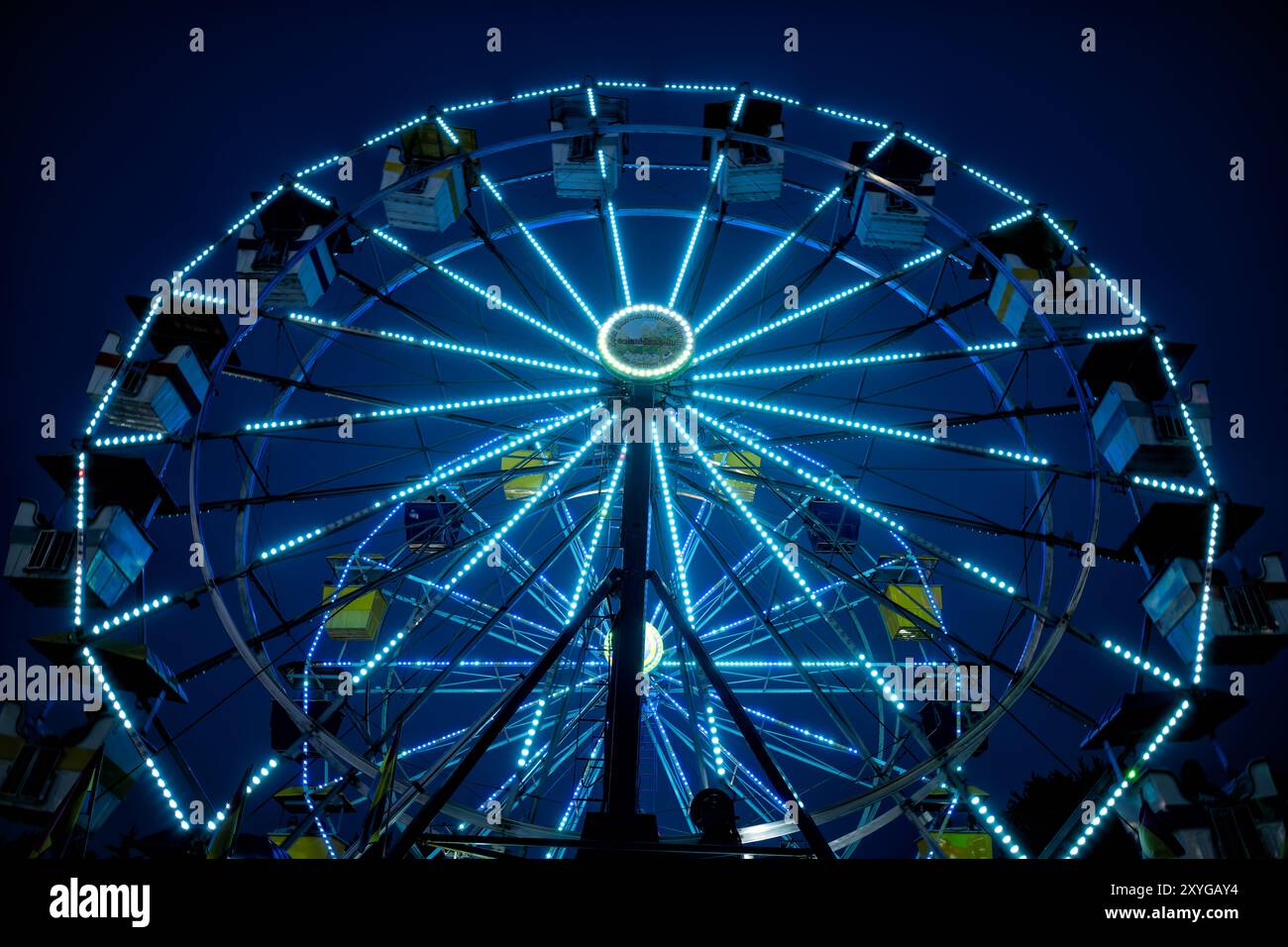 Ferris Wheel Arlington Virginia // ARLINGTON, Virginia — Ein leuchtend beleuchtetes Riesenrad hebt sich auf der Arlington County Fair vor dem Abendhimmel hervor. Die farbenfrohen Lichter des Rades sorgen für eine blendende Präsentation, die die festliche Atmosphäre der Messe einfängt, wenn der Tag in die Nacht verwandelt wird. Diese legendäre Karnevalsfahrt dient als Herzstück des jährlichen Gemeindeereignisses und bietet sowohl aufregende Ausblicke für Fahrer als auch eine malerische Szene für Märchenbesucher. Stockfoto