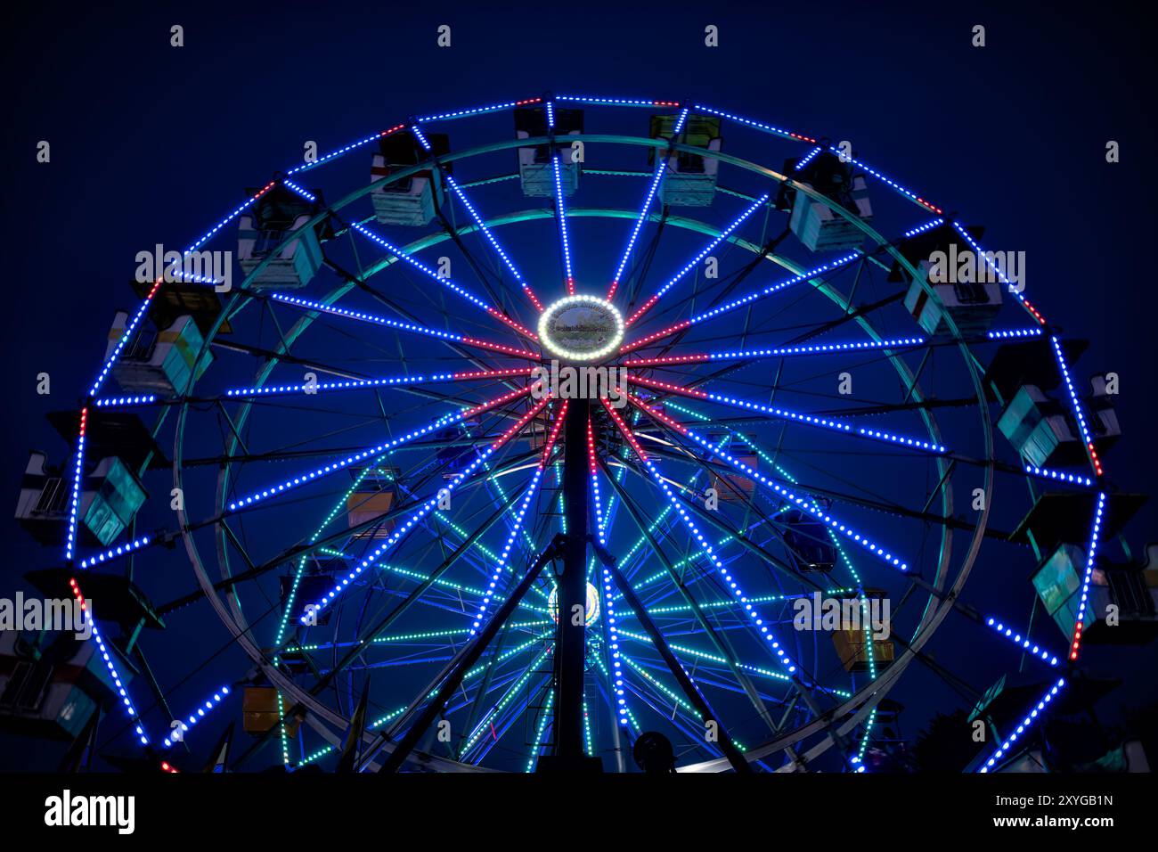 Arlington Virginia // ARLINGTON, Virginia — Ein leuchtend beleuchtetes Riesenrad hebt sich auf der Arlington County Fair vor dem Abendhimmel hervor. Die farbenfrohen Lichter des Rades sorgen für eine blendende Präsentation, die die festliche Atmosphäre der Messe einfängt, wenn der Tag in die Nacht verwandelt wird. Diese legendäre Karnevalsfahrt dient als Herzstück des jährlichen Gemeindeereignisses und bietet sowohl aufregende Ausblicke für Fahrer als auch eine malerische Szene für Märchenbesucher. Stockfoto