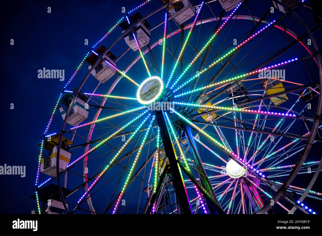 Arlington Virginia // ARLINGTON, Virginia — Ein leuchtend beleuchtetes Riesenrad hebt sich auf der Arlington County Fair vor dem Abendhimmel hervor. Die farbenfrohen Lichter des Rades sorgen für eine blendende Präsentation, die die festliche Atmosphäre der Messe einfängt, wenn der Tag in die Nacht verwandelt wird. Diese legendäre Karnevalsfahrt dient als Herzstück des jährlichen Gemeindeereignisses und bietet sowohl aufregende Ausblicke für Fahrer als auch eine malerische Szene für Märchenbesucher. Stockfoto