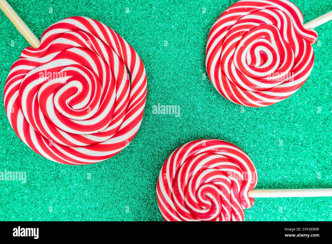 Drei Weihnachts-Lollypops vor grüner und glitzernder Kulisse. Hintergrundbild zu Weihnachten mit Kopierraum für Text. Stockfoto