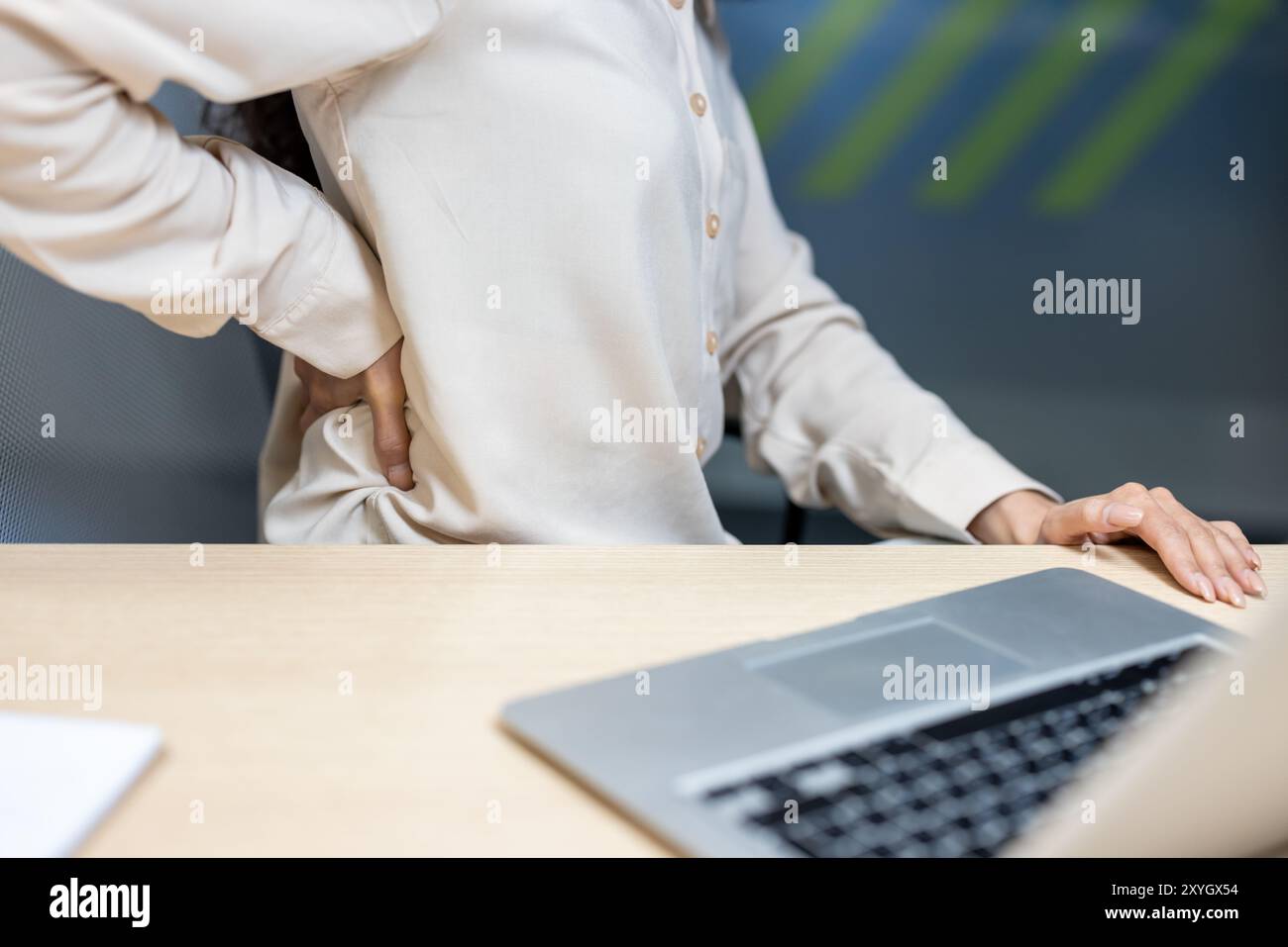 Büroangestellter fühlt sich unwohl, während er am Schreibtisch sitzt und Rückenschmerzen hat. Die Person drückt auf den unteren Rücken, um die Belastung oder Muskelschmerzen zu lindern. Das Bild zeigt häufige arbeitsbezogene Gesundheitsprobleme. Stockfoto