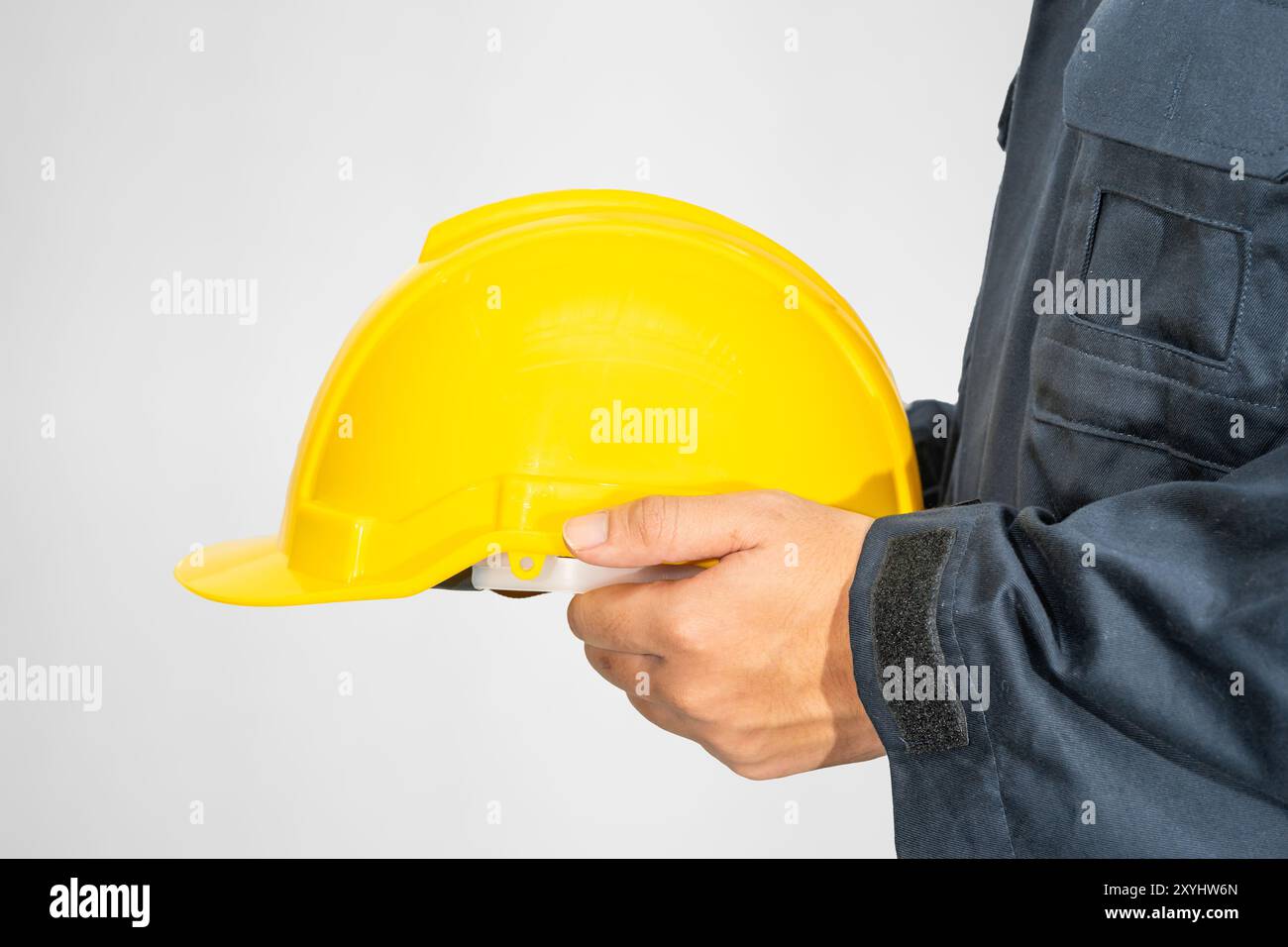 Verstopft Arbeiter, der in blauer Umhüllung steht und gelben Hardhut hält Isoliert auf grauem Hintergrund Stockfoto