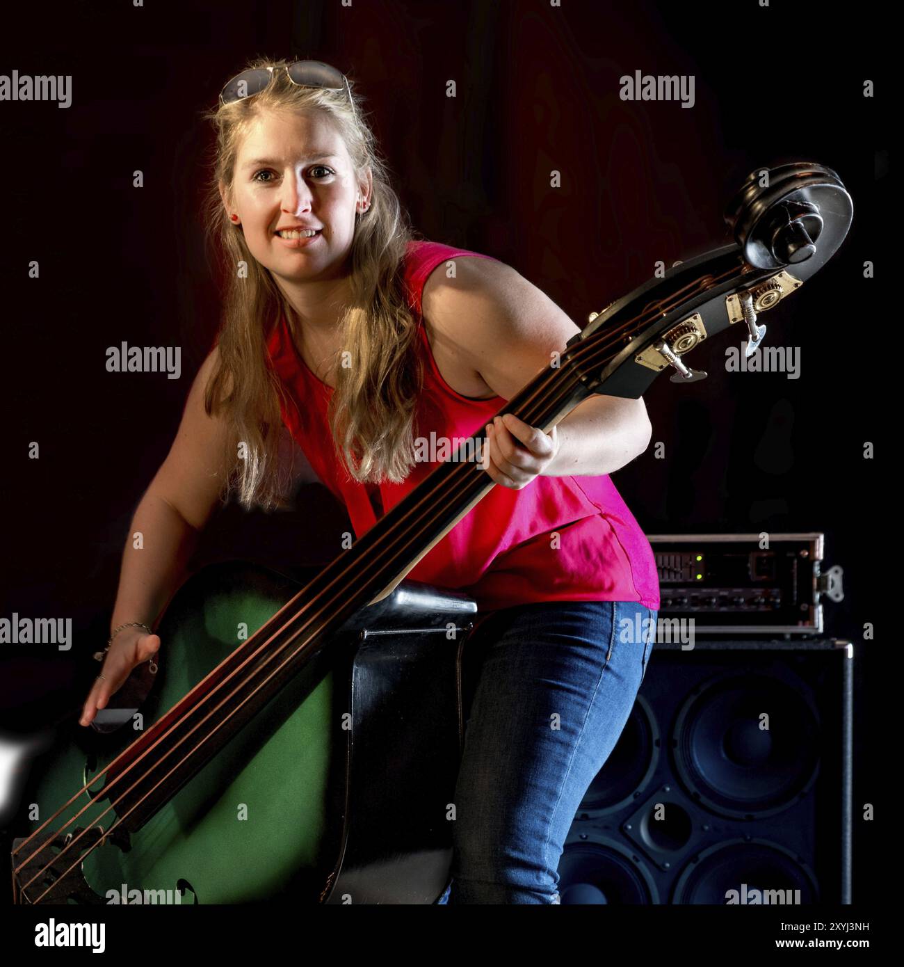 Musiker mit rotem Hemd spielt einen Kontrabass vor schwarzem Hintergrund Stockfoto