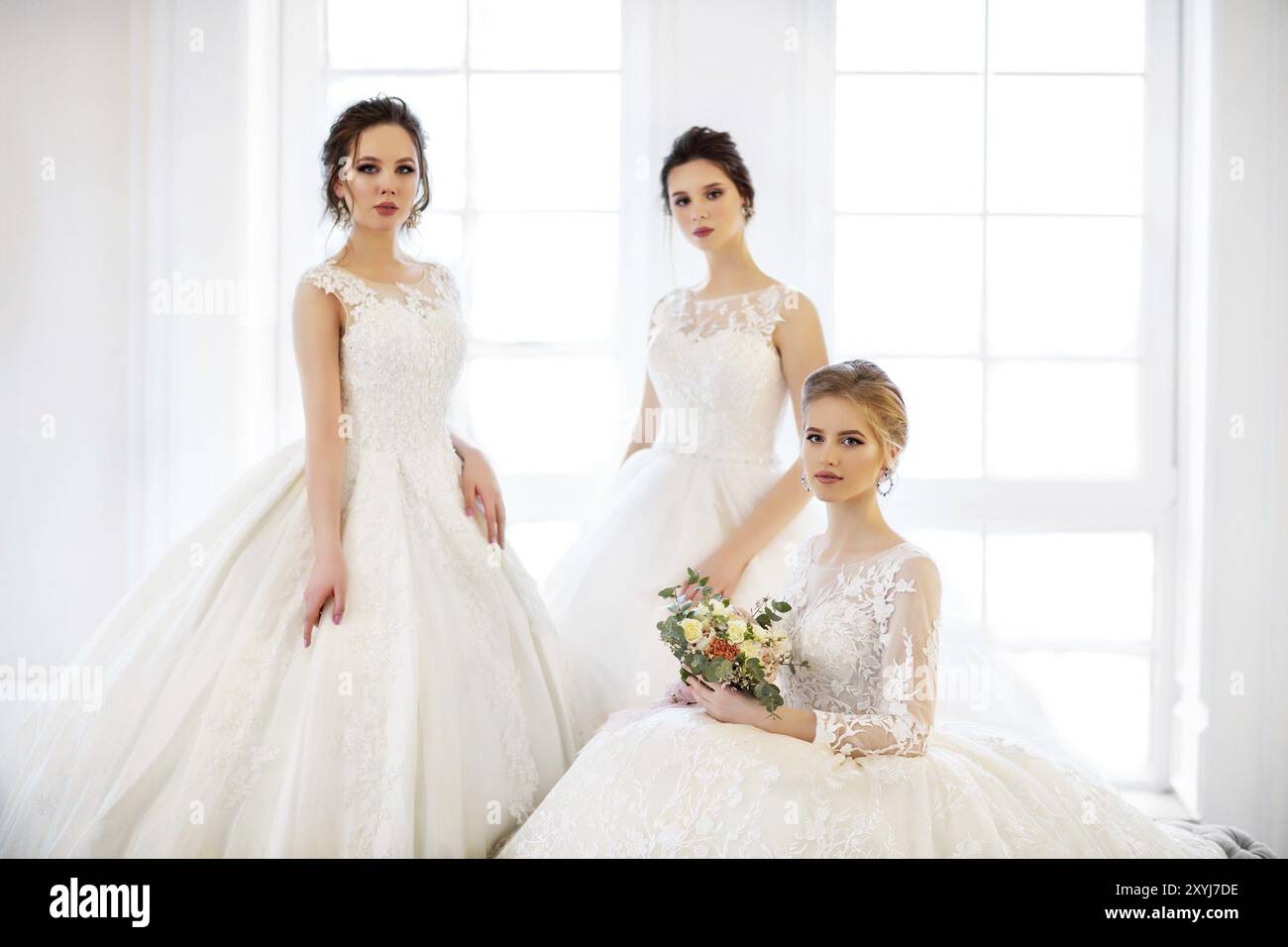 Drei junge Frau mit Blumensträuße tragen Brautkleider Stockfoto