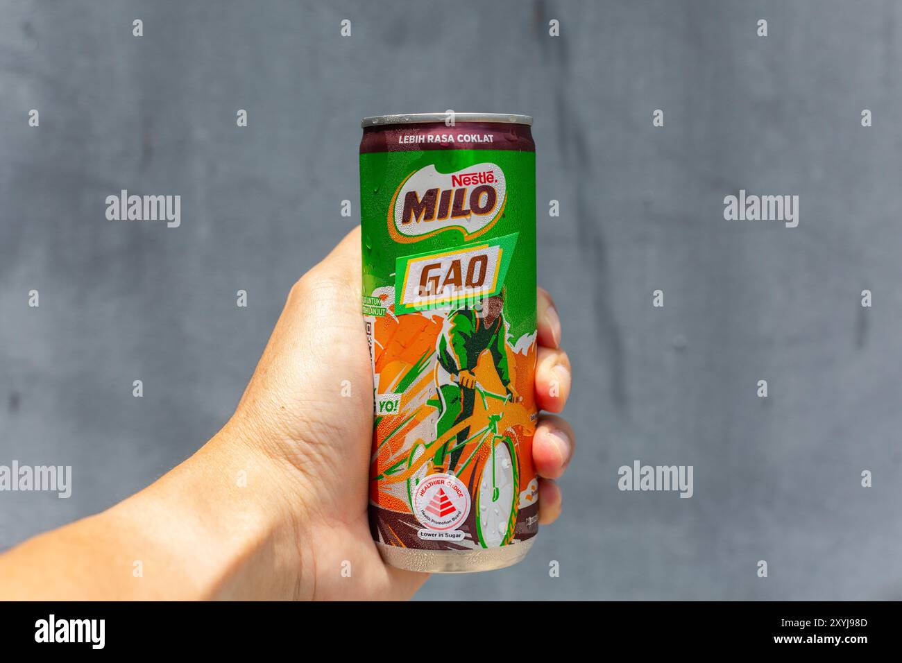 Die linke Hand hält das Getränk Nestlé Milo Gao vor grauem Hintergrund, eine dickere Version des Schokoladenmalzgetränks als die Standardversion. Stockfoto