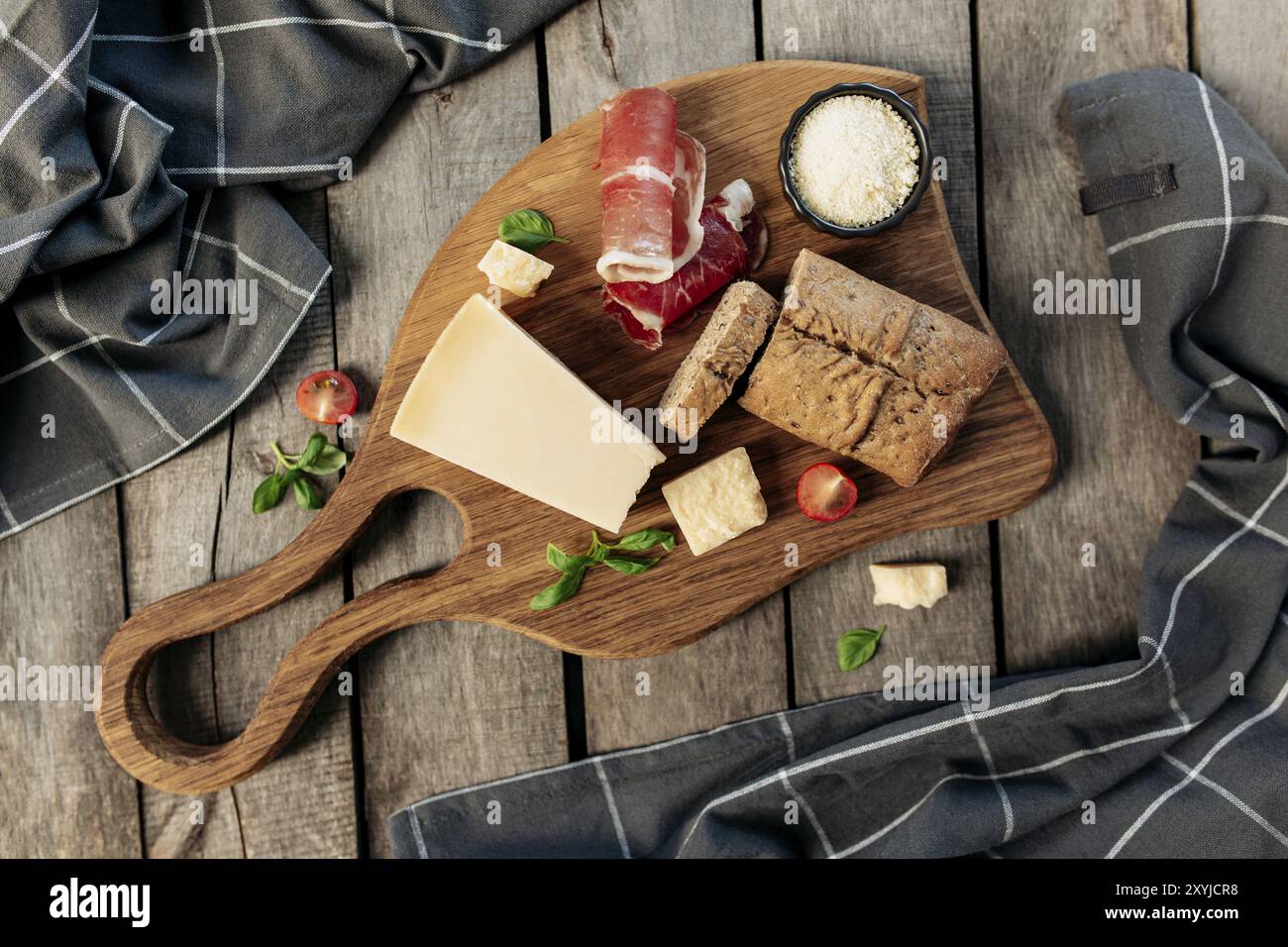 Italienische Küche Konzept flach Lay. Schneidebrett, Parmesan-Käsestückchen, geriebener Käse in schwarzer Schüssel, dünn geschnittener Schinken, Kirschtomate, Basilikumblätter b Stockfoto