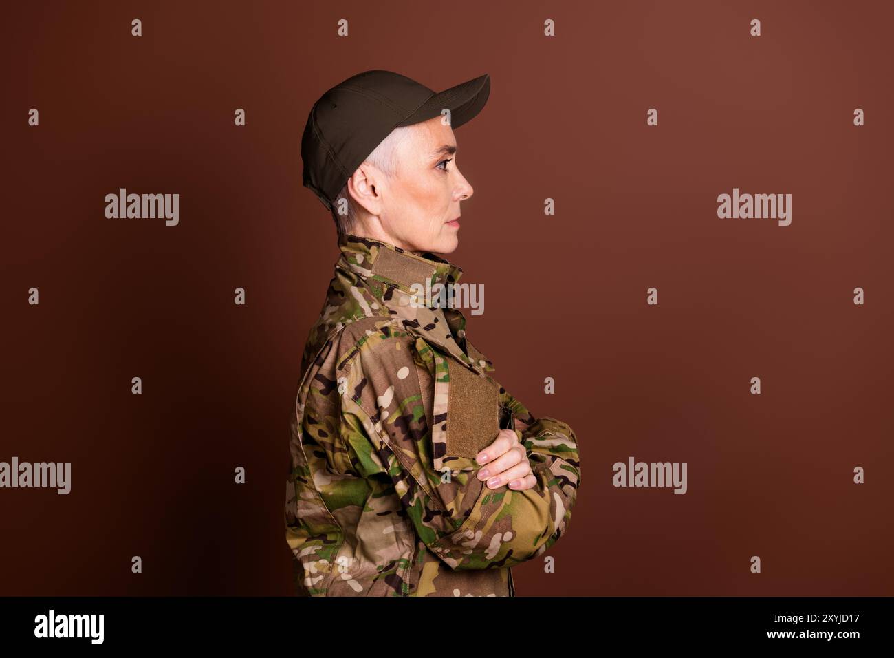 Foto einer starken ernsten älteren Dame gekleidet Camo Uniform Arme gefaltet aussehenden leeren Raum isolierter brauner Hintergrund Stockfoto