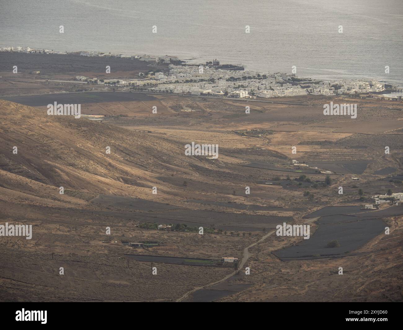 Küstenlandschaft mit Wüstendünen und einem kleinen weißen Dorf am Meer, Lanzarote, Kanarische Inseln, Spanien, Europa Stockfoto