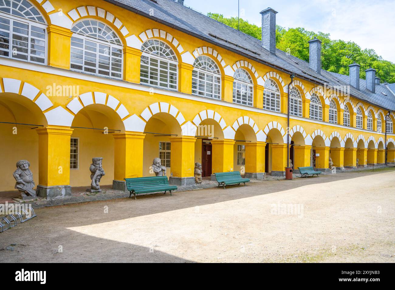 Hell gelber Innenhof des Chateau Velke Losiny in Tschechien, umgeben von charmanter Architektur und einladenden Bänken, genießen Sie die ruhige Atmosphäre an einem sonnigen Tag. Stockfoto