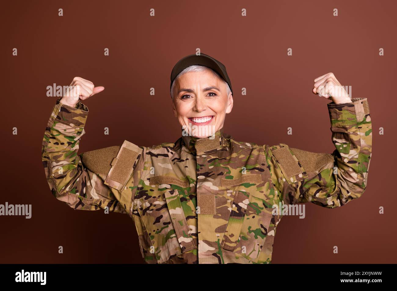 Foto von militärisch selbstbewusster Senior Frau trägt Camouflage aufsteigende Fäuste, die Muskeln leeren Raum isolierten braunen Hintergrund zeigen Stockfoto