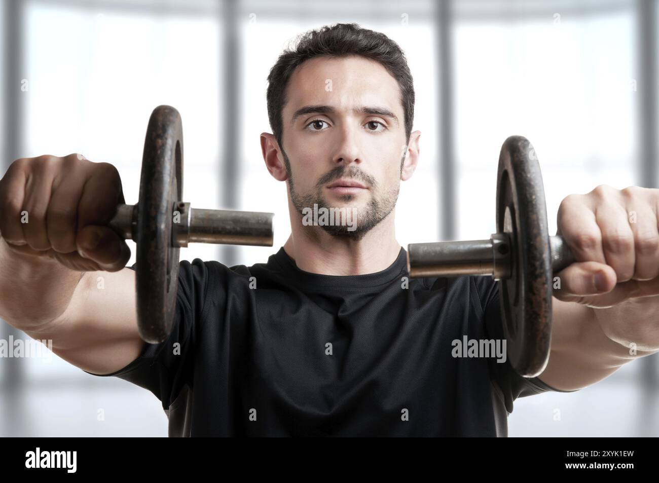 Personal Trainer tun vorderen Dumbell wirft für die Ausbildung seiner Deltamuskeln in braunem Hintergrund Stockfoto