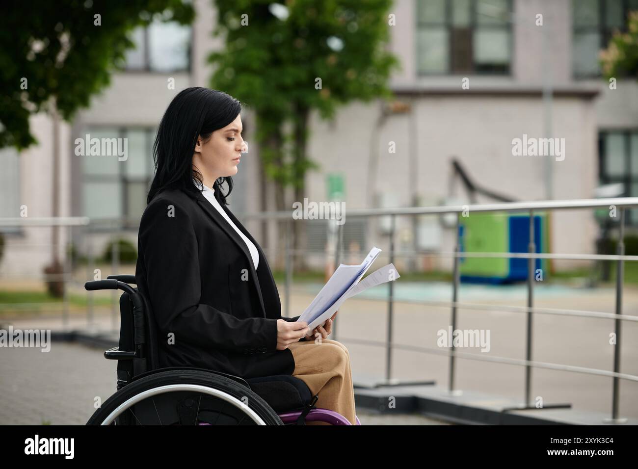 Eine Frau im Rollstuhl sitzt auf einem Bürgersteig und liest sich die Papiere durch. Stockfoto