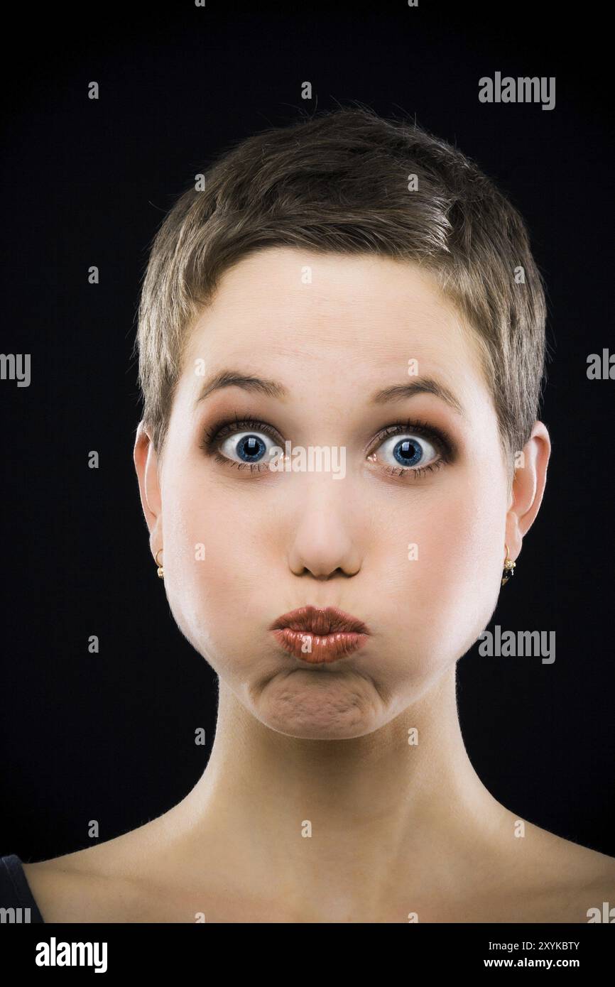 Hübsche Frau mit kurzen Haaren, die vor schwarzem Hintergrund Gesichter zieht Stockfoto