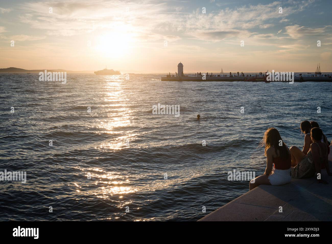 ZADAR, KROATIEN - 11. August 2024: Die Menschen an der Promenade bewundern den Sonnenuntergang der goldenen Stunde mit Blick auf die Adria, Zadar, Kroatien Stockfoto