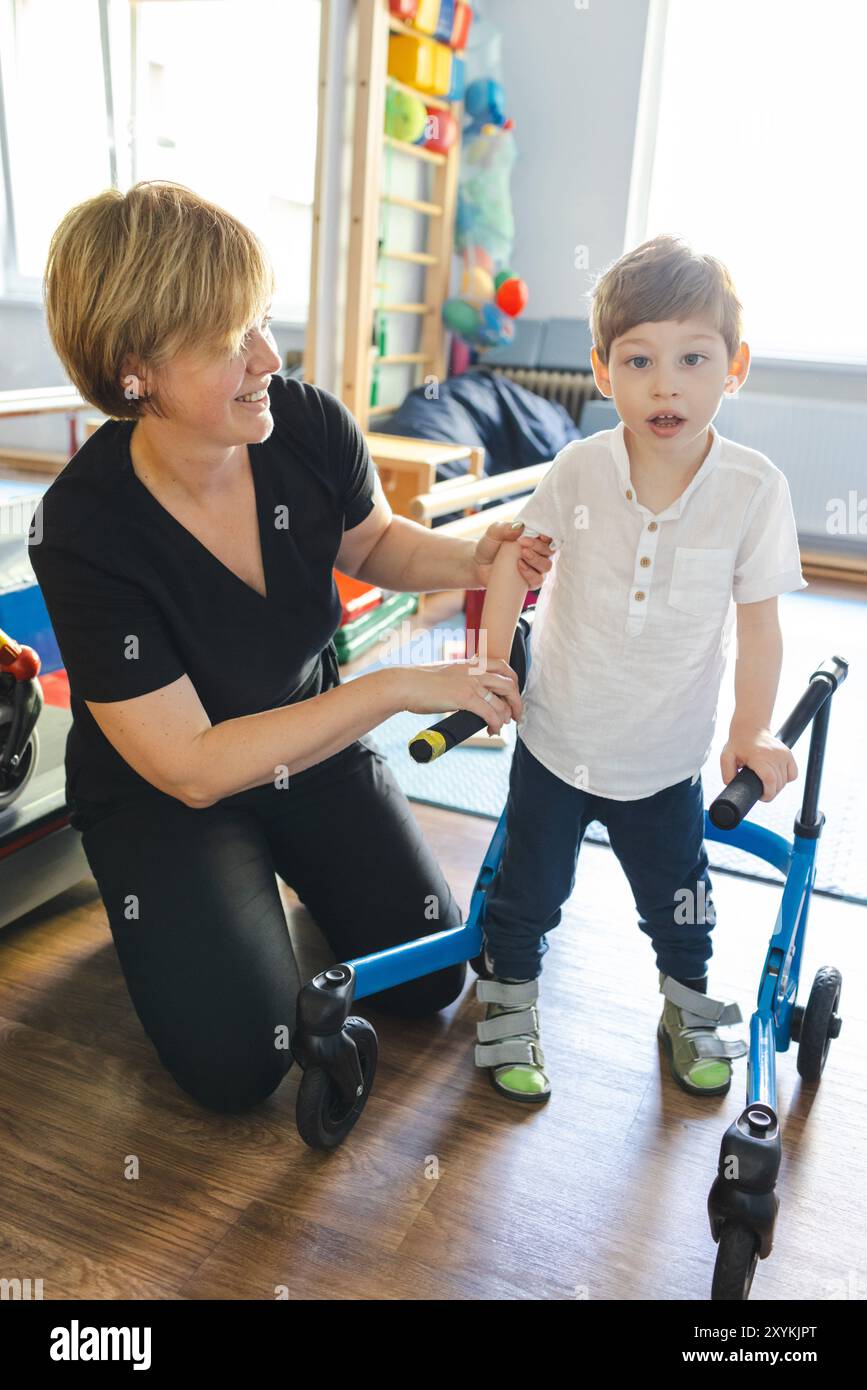 Der Physiotherapeut hilft einem Jungen mit Erkrankungen des Bewegungsapparates mit Mobilitätshilfen bei Rehabilitationsübungen in einer unterstützenden Umgebung Stockfoto