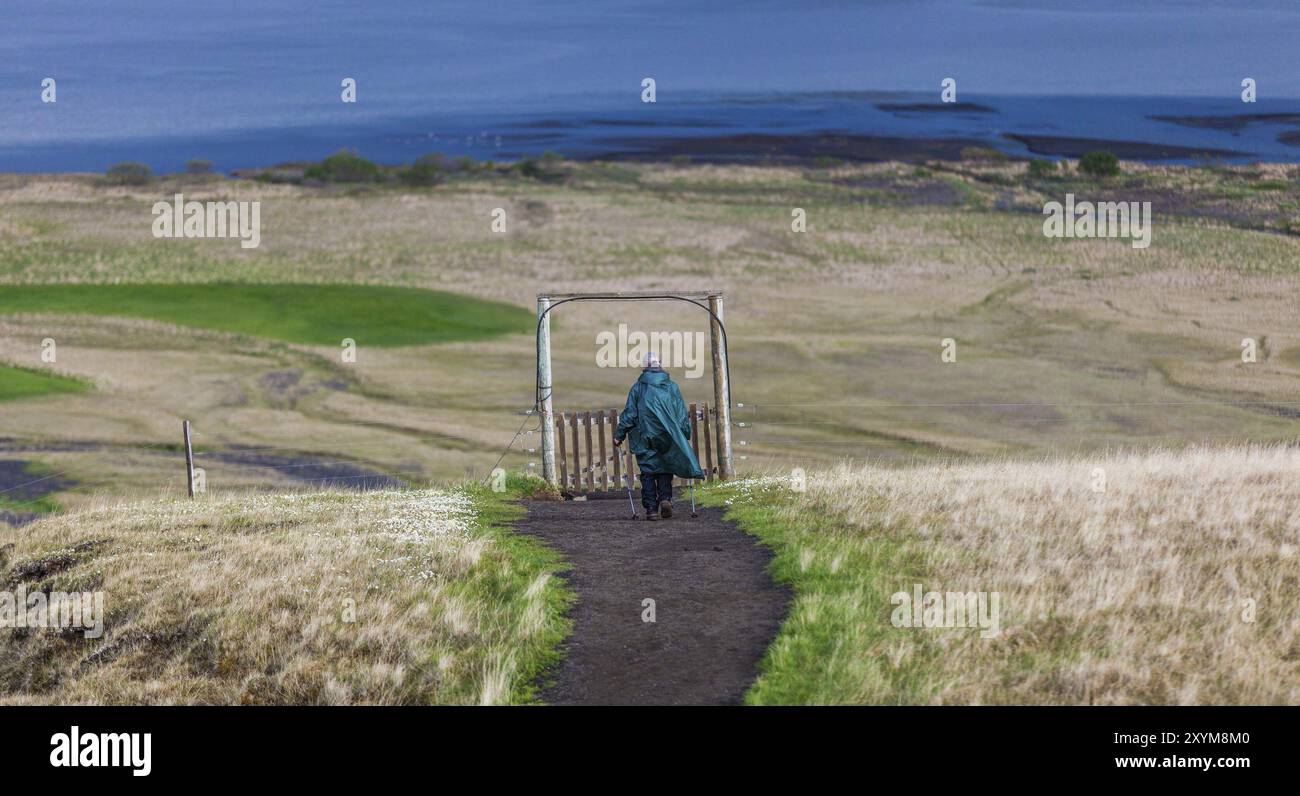 AUSTURLAND, ISLAND, 20. JUNI: Eine ältere Frau in einem grünen cape und mit Wanderstöcken wandert am 20. Juni 2013 in Austurla in der Nähe des Wasserfalls Hengifoss Stockfoto