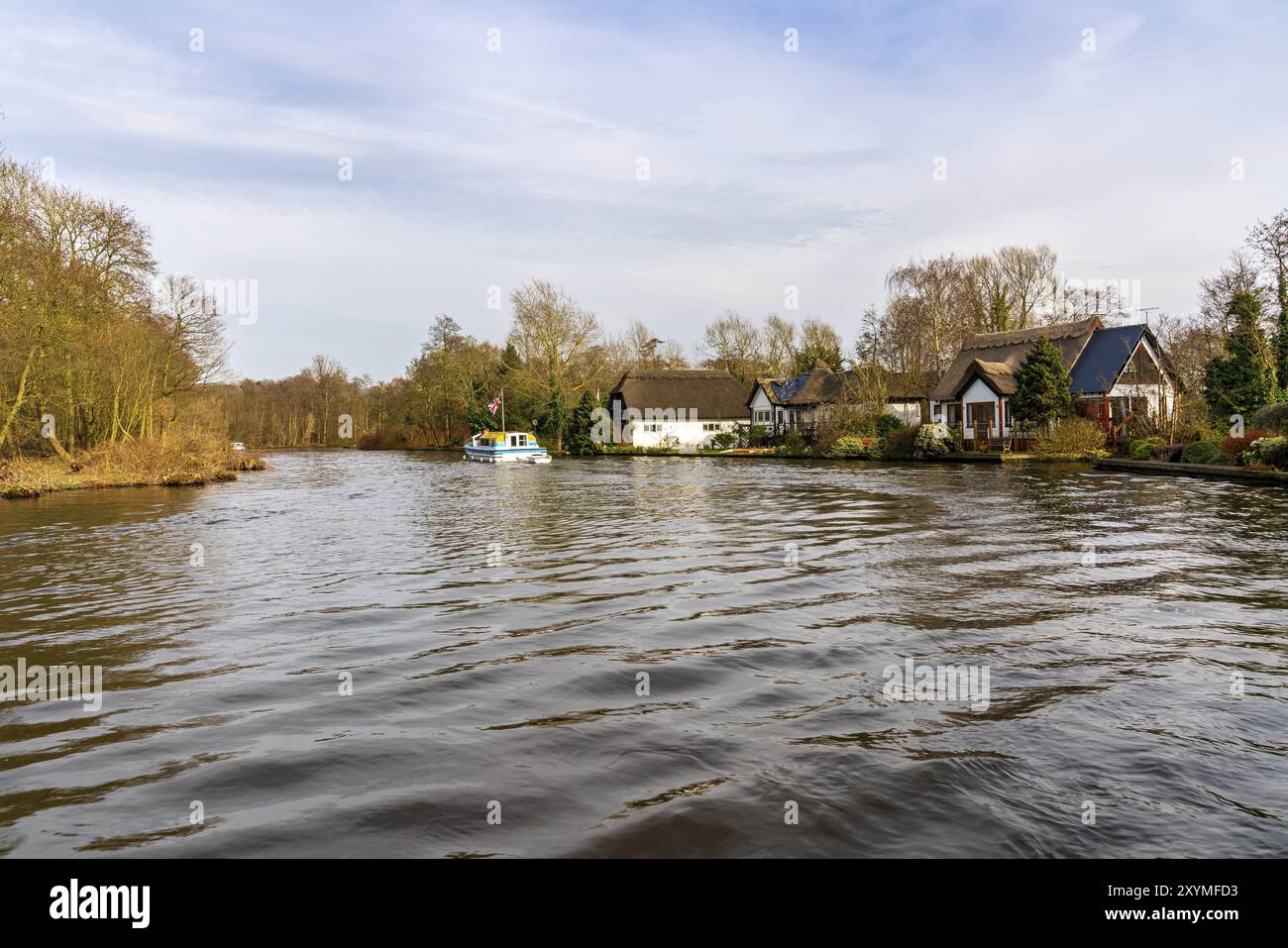 Wroxham, Norfolk, England, Vereinigtes Königreich, April 07, 2018: ein Boot auf dem Fluss Bure in den Broads mit Häusern von Wroxham am Ufer Stockfoto