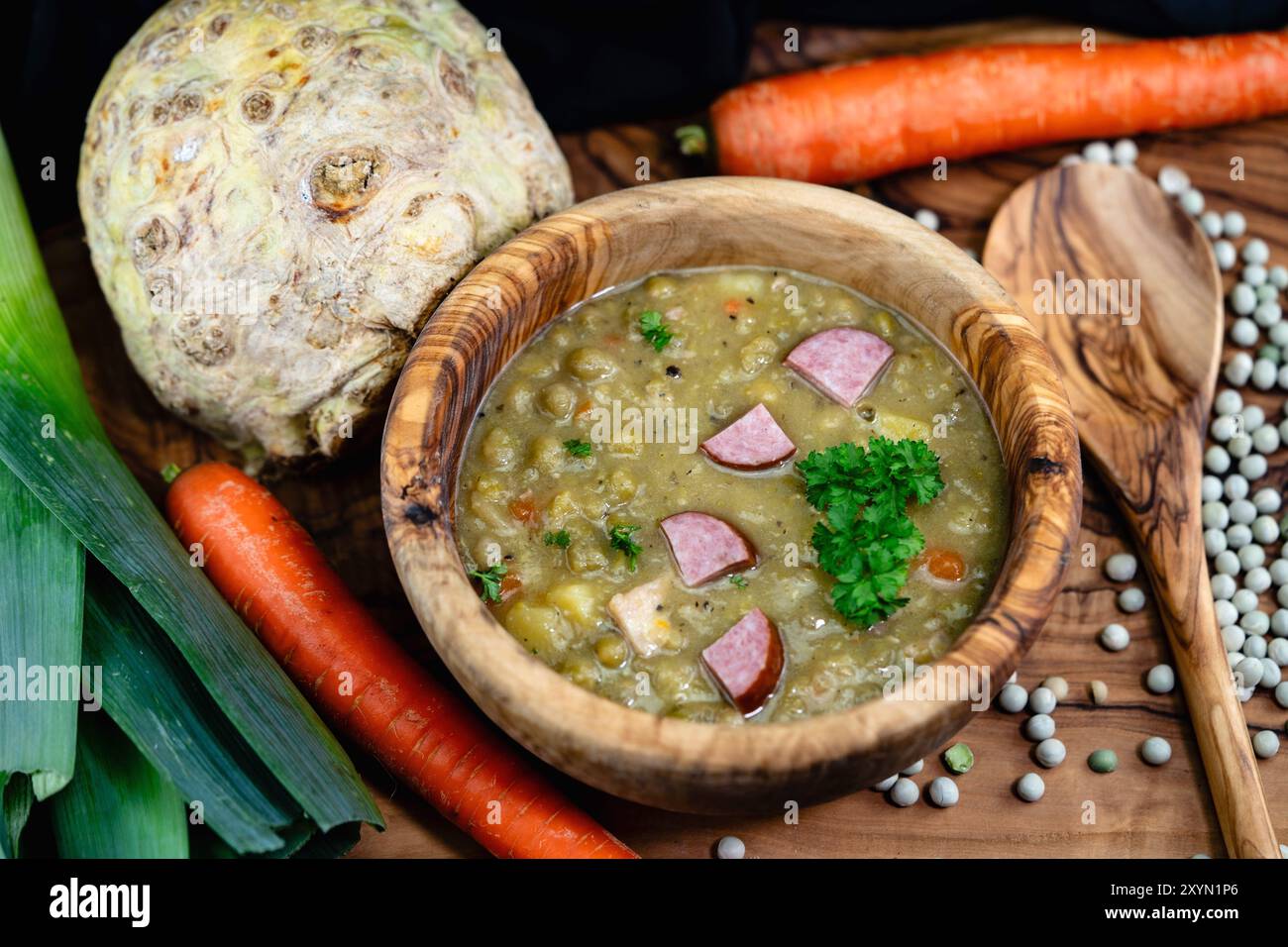 Holzschale mit Erbsensuppe und Wurst zwischen Karotten, Sellerie und Lauch Stockfoto