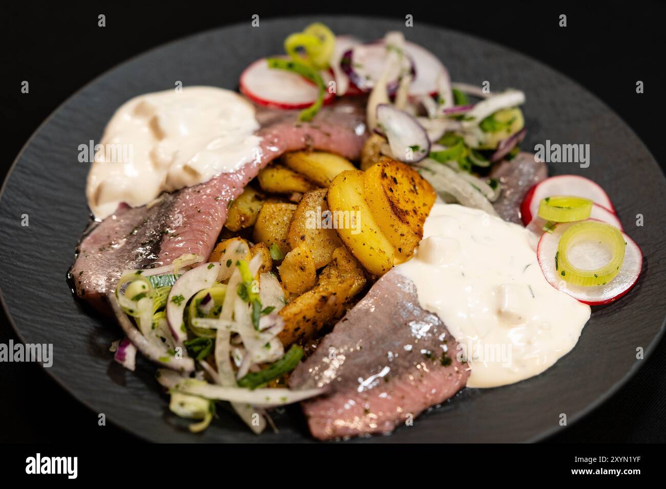 Matjes mit Remoulade, Zwiebeln und gebratenen Kartoffeln auf einem Teller Stockfoto
