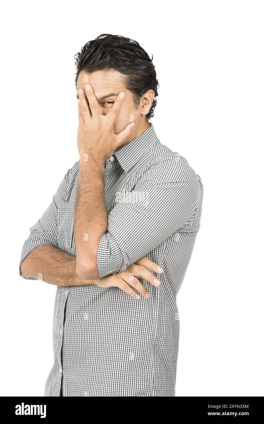 Profil eines gut aussehenden latino-Mannes in legeren Kleidern, Button-Down-Hemd, Hand bedeckendes Gesicht, Auge blickend durch gespaltenen Finger und zeigt schüchtern, feurig Stockfoto