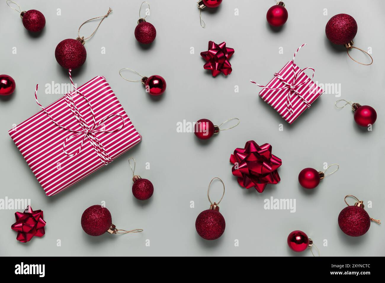 Grauer Hintergrund mit zwei rosa Weihnachts-Geschenkbox-Geschenken, kleinen roten Weihnachtskugeln oder Kugelspielzeug, Bandschleifen für Tannenbaum. Konzept für festliche Salbei Stockfoto