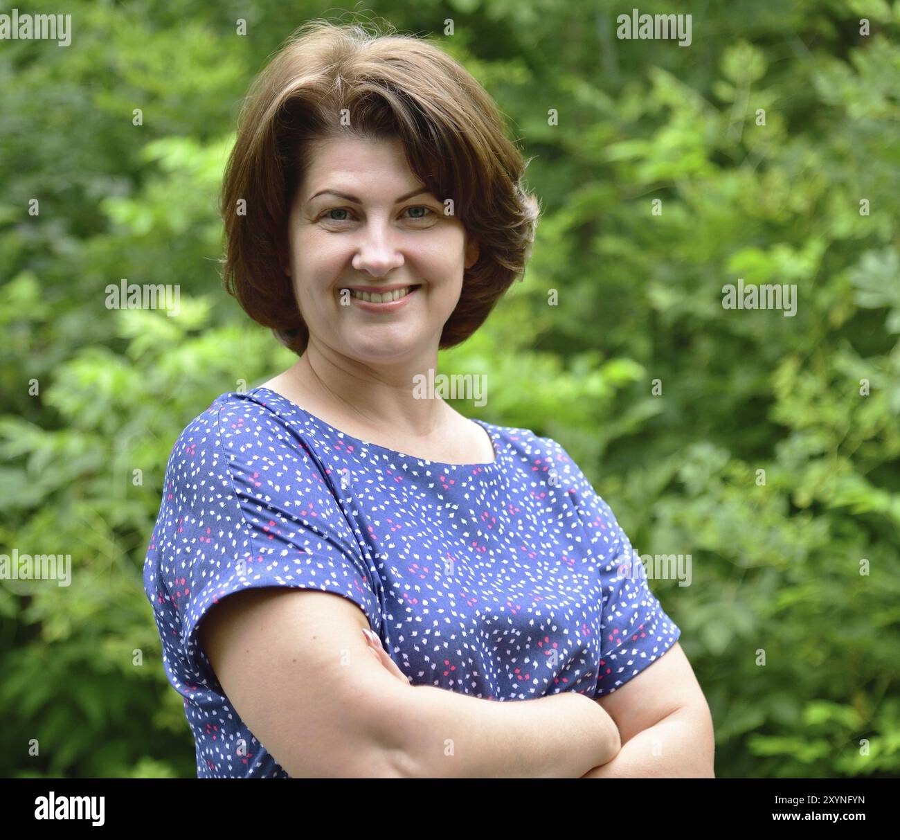 Lächelnde Frau in der Natur vor dem Hintergrund grüner Blätter Stockfoto