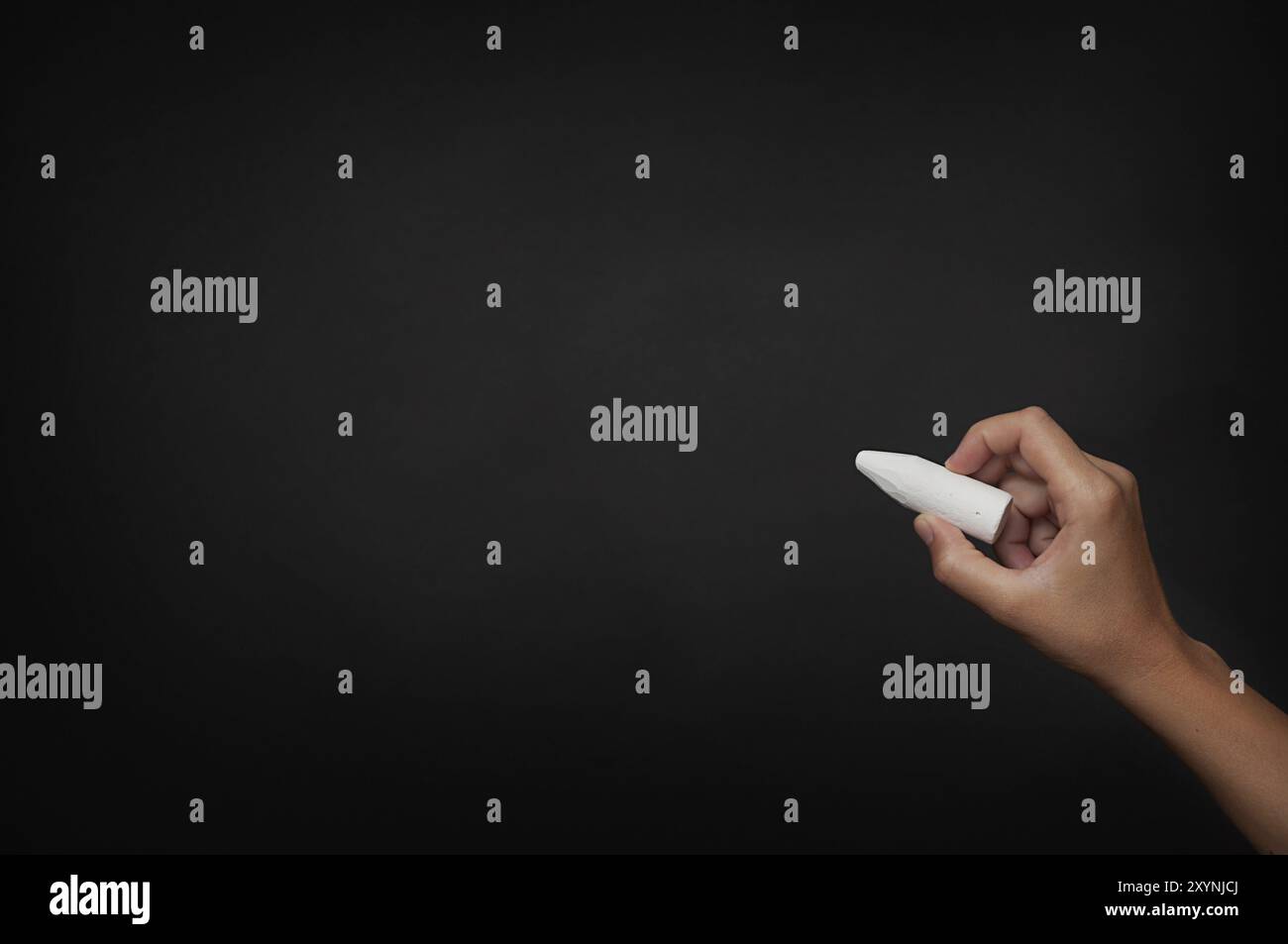 Hand mit weißem Stück Kreide über dunkler Tafel Stockfoto