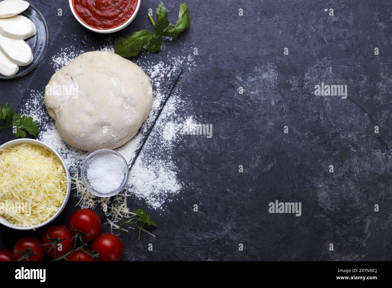 Rohen Teig für Pizza mit Zutaten und Gewürzen auf schwarzen background.overhead mit Textfreiraum Stockfoto