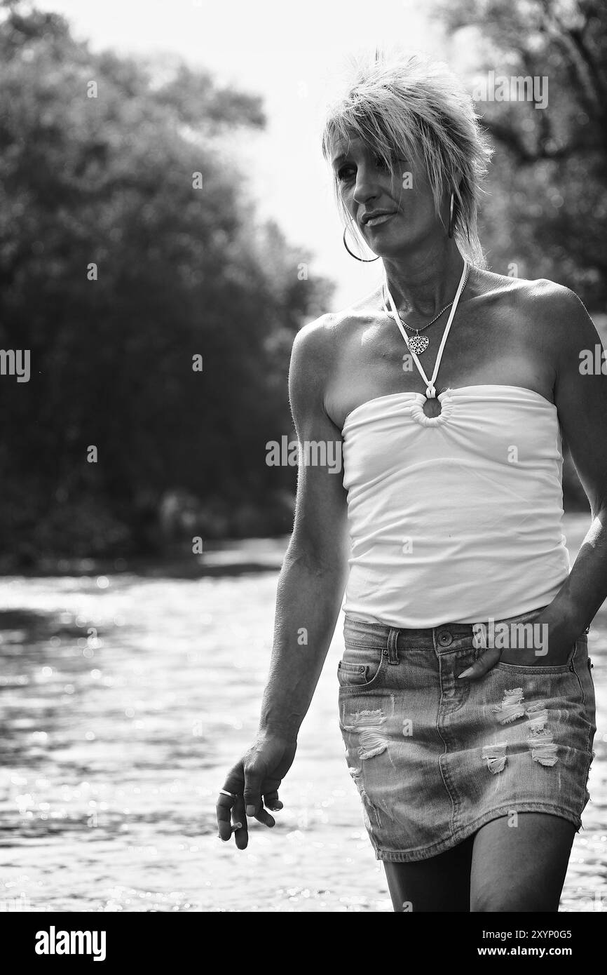 Eine Frau, die raucht und nachdenklich in einem Fluss läuft, die ganze Sache in Schwarz und weiß Stockfoto