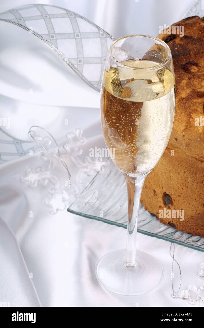 Panettone der italienische Weihnachtsgebäck serviert auf einem transparenten Glasteller, ein Glas Spumante und einige Ornamente. Selektiver Fokus Stockfoto